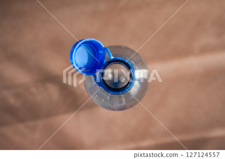 Open plastic bottle with attached new designed blue cap on wooden background in sunlight Open plastic bottle with attached new designed blue cap on wooden background in sunlight 127124557