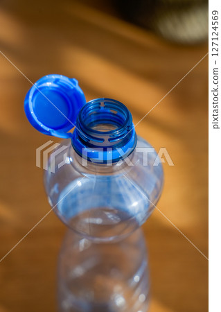 Open plastic bottle with attached blue cap on wooden background in sunlight Open plastic bottle with attached blue cap on wooden background in sunlight 127124569