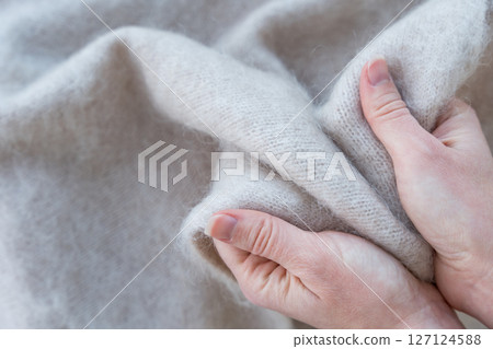 Hands holding soft white mohair wool fabric, showcasing texture and warmth Hands holding soft white mohair wool fabric, showcasing texture and warmth 127124588