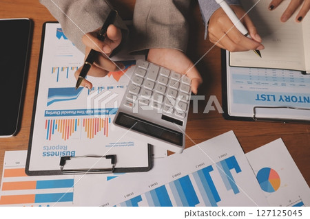 Group of confident business people point to graphs and charts to analyze market data, balance sheet, account, net profit to plan new sales strategies to increase production capacity. 127125045