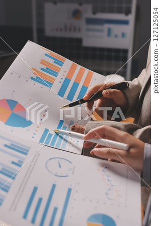 Group of confident business people point to graphs and charts to analyze market data, balance sheet, account, net profit to plan new sales strategies to increase production capacity. 127125054