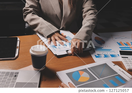 Group of confident business people point to graphs and charts to analyze market data, balance sheet, account, net profit to plan new sales strategies to increase production capacity. 127125057