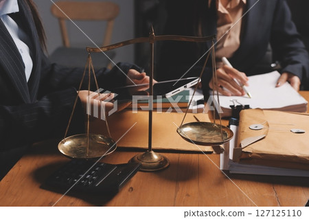 Attractive young lawyer in office Business woman and lawyers discussing contract papers with brass scale on wooden desk in office. Law, legal services, advice, Justice and real estate concept. 127125110