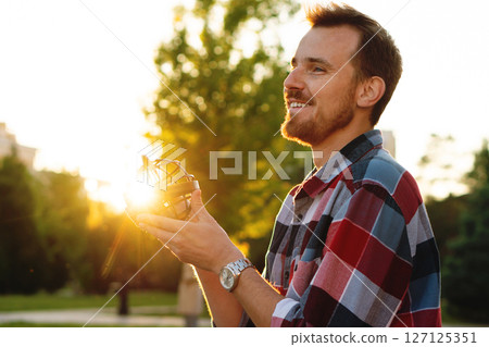 Smiling young man holding globe illuminated by golden sunset 127125351