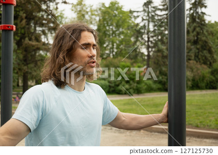 Portrait of tired sporty caucasian man thoughtful expression, lost in thought at public park near sport ground equipment. Laziness, forces himself to exercise. Slow living. Outdoor Portrait of tired sporty caucasian man thoughtful expression, lost in thought at public park near sport ground equipment. Laziness, forces himself to exercise. Slow living. Outdoor 127125730