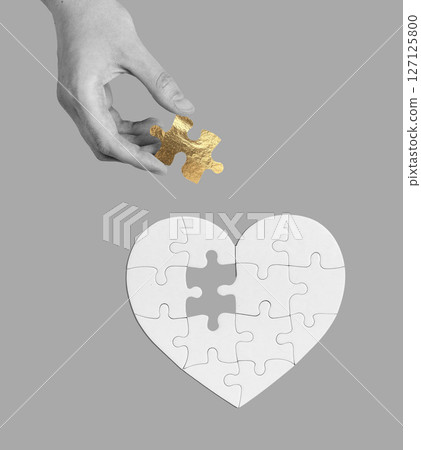 Hand holding a golden heart puzzle piece, symbolizing love, connection, and emotional healing. 127125800