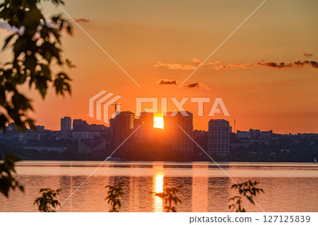 Sunset over modern city skyline and calm river surface. Sunset over modern city skyline and calm river surface. 127125839