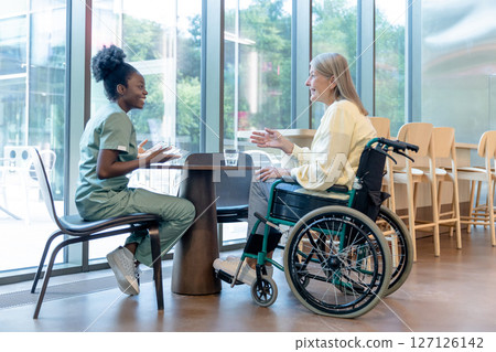 Doctor and patient on a wheelchair talking and looking peaceful 127126142