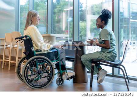 Doctor and patient on a wheelchair talking and looking peaceful 127126143