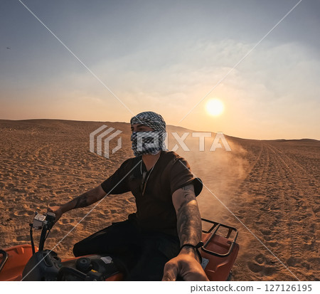 Tourist riding quad bike and taking selfie in desert at sunset 127126195