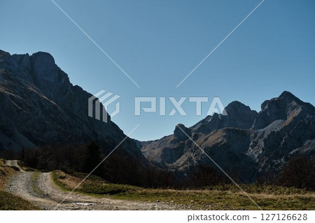 Grassy trail at the foot of Komovi peaks in Montenegro. Peaceful autumn landscape with dramatic alpine backdrop under a deep blue sky. Grassy trail at the foot of Komovi peaks in Montenegro. Peaceful autumn landscape with dramatic alpine backdrop under a deep blue sky. 127126628