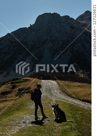Woman hiking with two dogs - German and Australian shepherds on a mountain trail in the Komovi range, Montenegro, surrounded by dramatic peaks and golden autumn meadows. Hiking with pet concept Woman hiking with two dogs - German and Australian shepherds on a mountain trail in the Komovi range, Montenegro, surrounded by dramatic peaks and golden autumn meadows. Hiking with pet concept 127126631