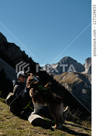Smiling woman sitting with two dogs on a bench in the Komovi mountains of Montenegro, enjoying a sunny autumn day with stunning rocky peaks in the background. Hiking with pet concept Smiling woman sitting with two dogs on a bench in the Komovi mountains of Montenegro, enjoying a sunny autumn day with stunning rocky peaks in the background. Hiking with pet concept 127126655