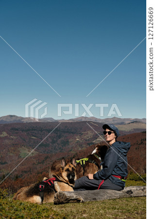 Woman sits on a log with two dogs. German and Australian Shepherds, enjoying peaceful autumn day in Montenegro Komovi mountains with owner. The moment captures loyalty and serenity Woman sits on a log with two dogs. German and Australian Shepherds, enjoying peaceful autumn day in Montenegro Komovi mountains with owner. The moment captures loyalty and serenity 127126669