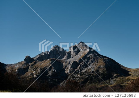 Dramatic rocky peak of Komovi mountain range in Montenegro under a clear blue sky. Majestic and rugged alpine scenery captured in crisp autumn light Dramatic rocky peak of Komovi mountain range in Montenegro under a clear blue sky. Majestic and rugged alpine scenery captured in crisp autumn light 127126698