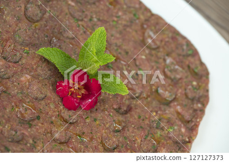 Delicious Lebanese Kebbe Naye garnished with olive oil and fresh mint on a rustic wooden table 127127373