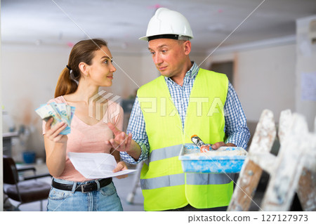 Woman owner of apartment giving wage to man construction painter 127127973