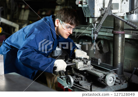 Young worker operating industrial drill press in metal workshop Young worker operating industrial drill press in metal workshop 127128049