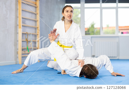 Young woman wearing kimono applying arm twist technique against middle-aged man Young woman wearing kimono applying arm twist technique against middle-aged man 127128066