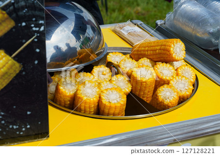 Freshly grilled corn cobs on display at a vibrant outdoor market event Freshly grilled corn cobs on display at a vibrant outdoor market event 127128221