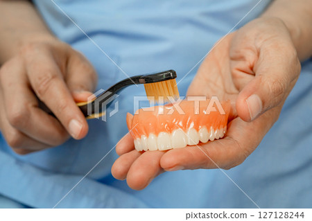 Asian senior woman patient clean teeth denture with toothbrush for chew food. Asian senior woman patient clean teeth denture with toothbrush for chew food. 127128244