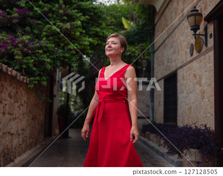 Woman in red dress walking narrow streets of old town Antalya during warm summer evening. Historic atmosphere and Mediterranean charm creates peaceful travel experience. 127128505