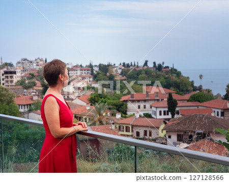 Woman in red dress walking narrow streets of old town Antalya during warm summer evening. Historic atmosphere and Mediterranean charm creates peaceful travel experience. view on Kalechi 127128566