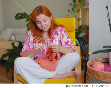 Young Woman knitting scarf in living room. doing crochet knits. 127128567