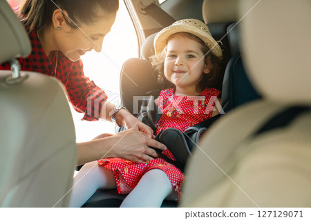 Smiling happy mother fastening her daughter in child car seat. Smiling happy mother fastening her daughter in child car seat. 127129071