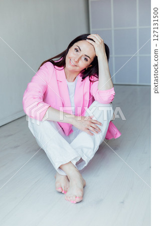 Beautiful brunette woman in white clothes and pink jacket sitting on the floor 127131500