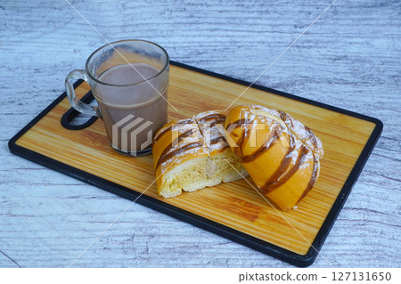 A sliced mocha golden loaf with chocolate drizzle and powdered sugar, served with a glass of hot chocolate on a wooden board. A sliced mocha golden loaf with chocolate drizzle and powdered sugar, served with a glass of hot chocolate on a wooden board. 127131650