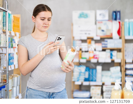 Pregnant woman in pharmacy scans QR code on shampoo 127131709