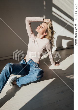 Beautiful slim blonde in jeans sitting on the floor 127131723