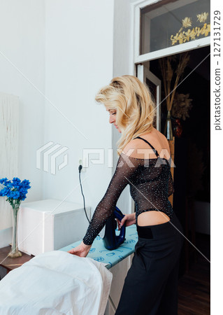 Beautiful fashionable blonde ironing clothes on a board 127131729