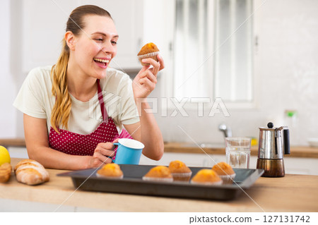 Cheerful young housewife tasting baked muffins at home 127131742