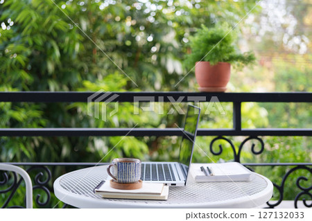 Afternoon tea break with a laptop on a white metal table, outdoor balcony view 127132033