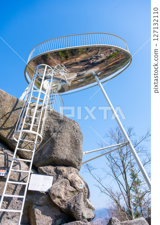 Visitors admire the panoramic views from Sipka lookout platform in the Jizera Mountains, with a bright blue sky and rocky terrain surrounding the structure, offering a unique vantage point. 127132110