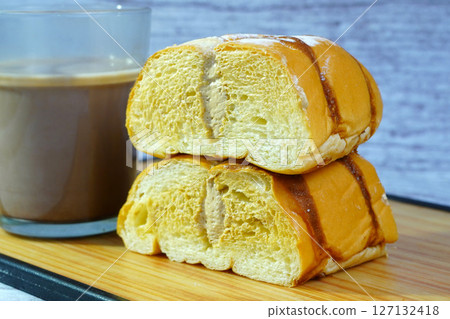 Close-up of sliced golden bread with chocolate drizzle and powdered sugar, filled with mocha cream, next to a mug of milk. Close-up of sliced golden bread with chocolate drizzle and powdered sugar, filled with mocha cream, next to a mug of milk. 127132418