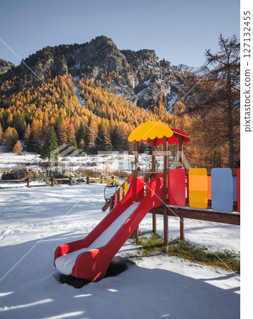 Colorful playground equipment contrasting snowy ground, autumnal trees, and mountain landscape in aosta, italian alpine region Frazionne Lillaz Colorful playground equipment contrasting snowy ground, autumnal trees, and mountain landscape in aosta, italian alpine region Frazionne Lillaz 127132455