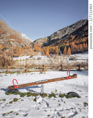 Snow covering wooden seesaw near mountain landscape, vibrant autumn foliage framing scenic valley in aosta, italy Frazionne Lillaz 127132463