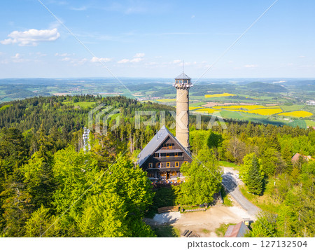 Explore the breathtaking aerial perspective of Svatobor Lookout Tower surrounded by lush greenery, offering panoramic views of the rolling hills and vibrant fields in Czechia. 127132504