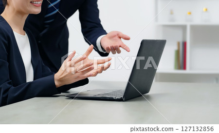 A group of male and female business people talking while looking at a laptop in an office A group of male and female business people talking while looking at a laptop in an office 127132856