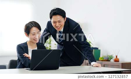 A group of male and female business people talking while looking at a laptop in an office A group of male and female business people talking while looking at a laptop in an office 127132857
