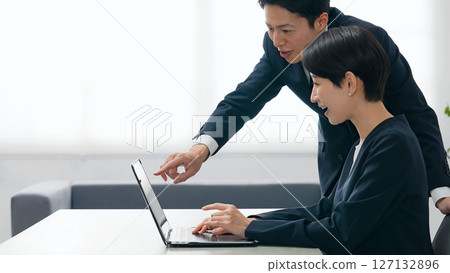 A group of male and female business people talking while looking at a laptop in an office A group of male and female business people talking while looking at a laptop in an office 127132896
