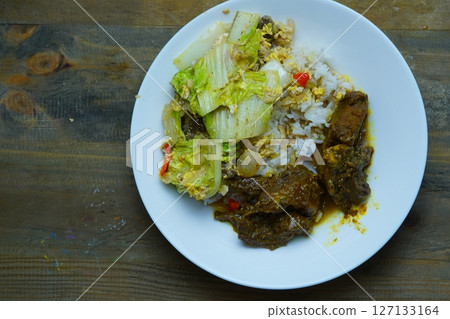 A plate of rice with beef rendang and stir-fried napa cabbage on a wooden table. A plate of rice with beef rendang and stir-fried napa cabbage on a wooden table. 127133164