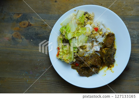 A plate of rice with beef rendang and stir-fried napa cabbage on a wooden table. A plate of rice with beef rendang and stir-fried napa cabbage on a wooden table. 127133165