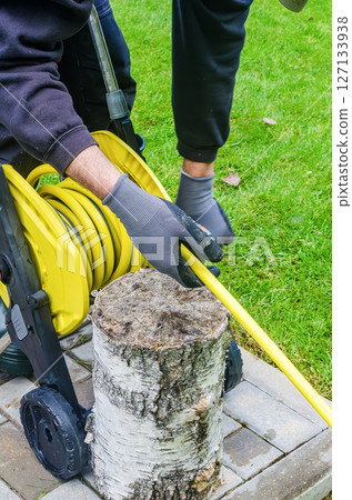 Winding yellow garden hose with gloves on a reel next to tree stump. High quality photo 127133938
