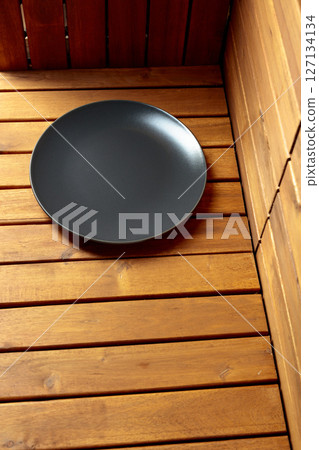 Empty black plate on natural wooden background. 127134134