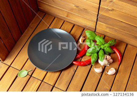 Empty black plate, garlic, basil, and red pepper on a natural wooden background. 127134136
