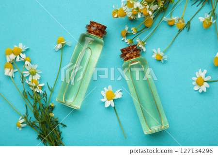 Bottles of essential oil and chamomile flowers on blue background 127134296